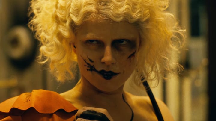 A woman with smudged black makeup and touseled wavy hair smirks.